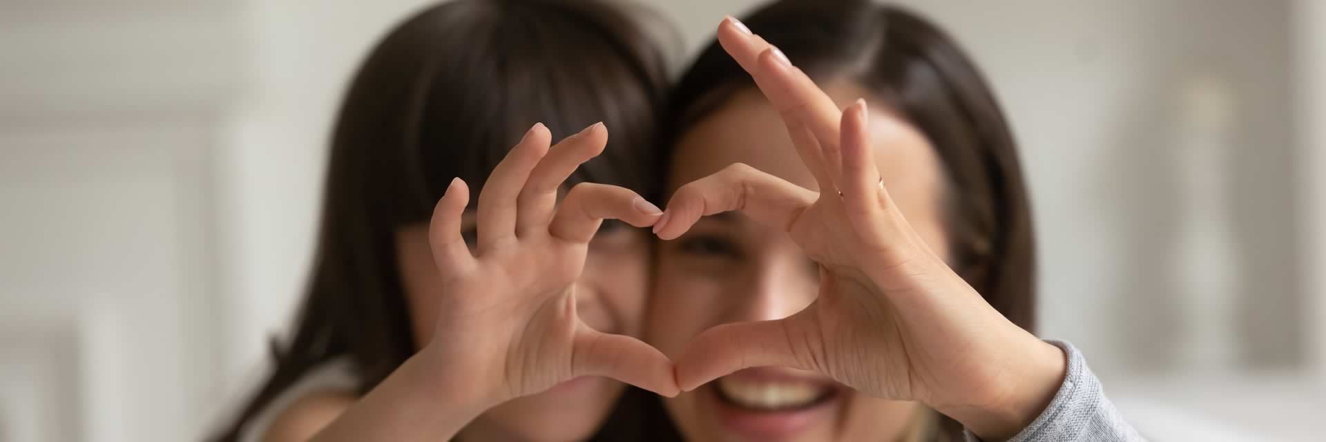 Happy young mother with adopted daughter making heart sign